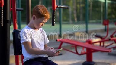 一个在街头公共健身器材上的男孩看着他的智能手机